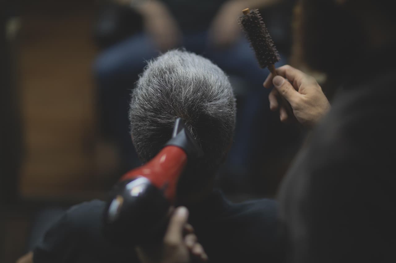 A barber blow-drying and brushing a customer's hair