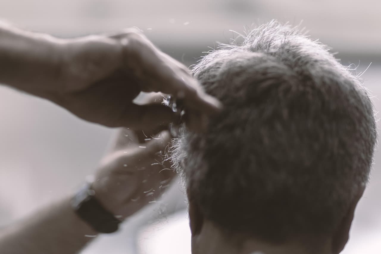 A barber's hands cutting short grey hair with scissors