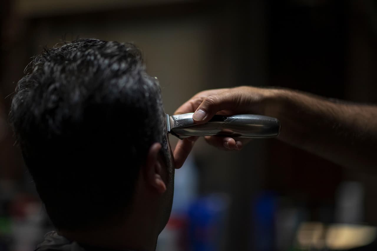 Clippers at the back of a customer's head in a dimly lit shop