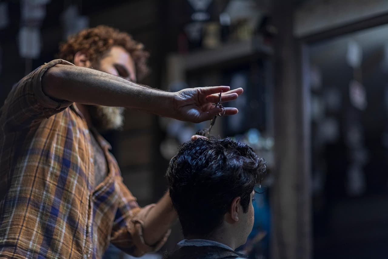 A barber cutting a young man's hair with scissors