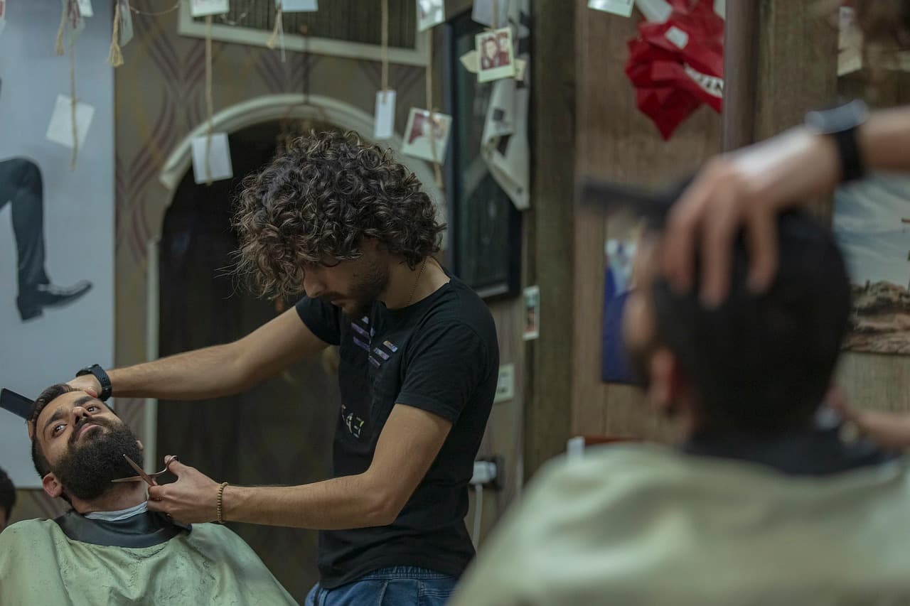 A barber trimming a customer's beard with clippers